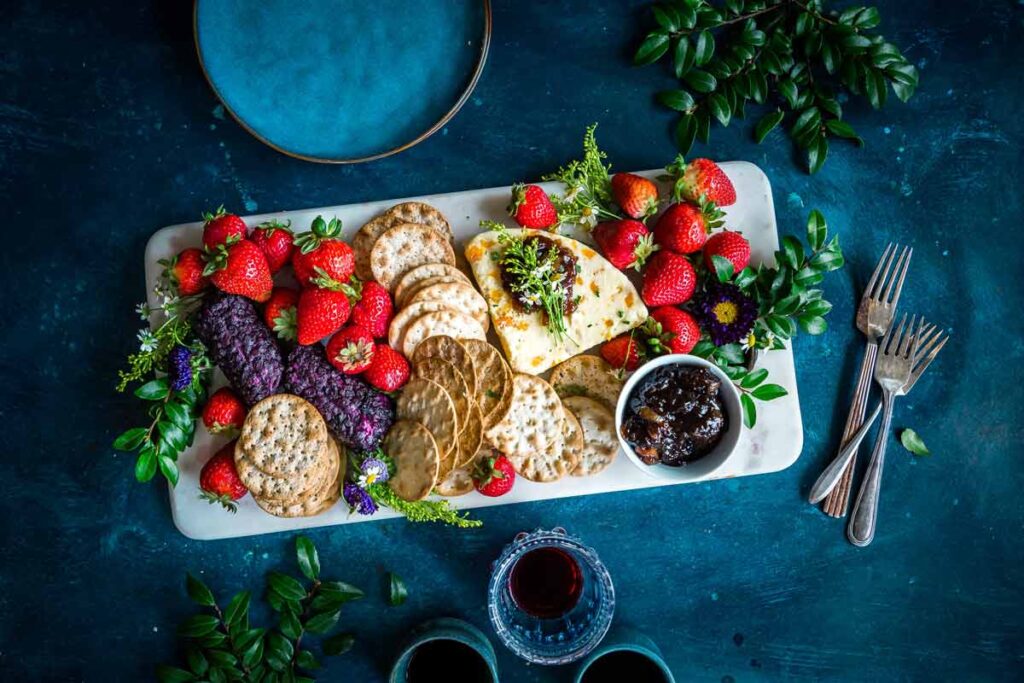 A charcuterie board with dates, strawberries, crackers, and cheese