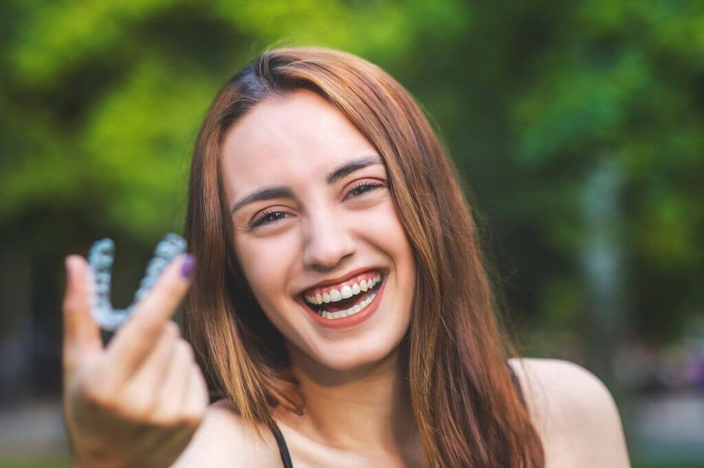 Smiling woman holding clear Invisalign aligners